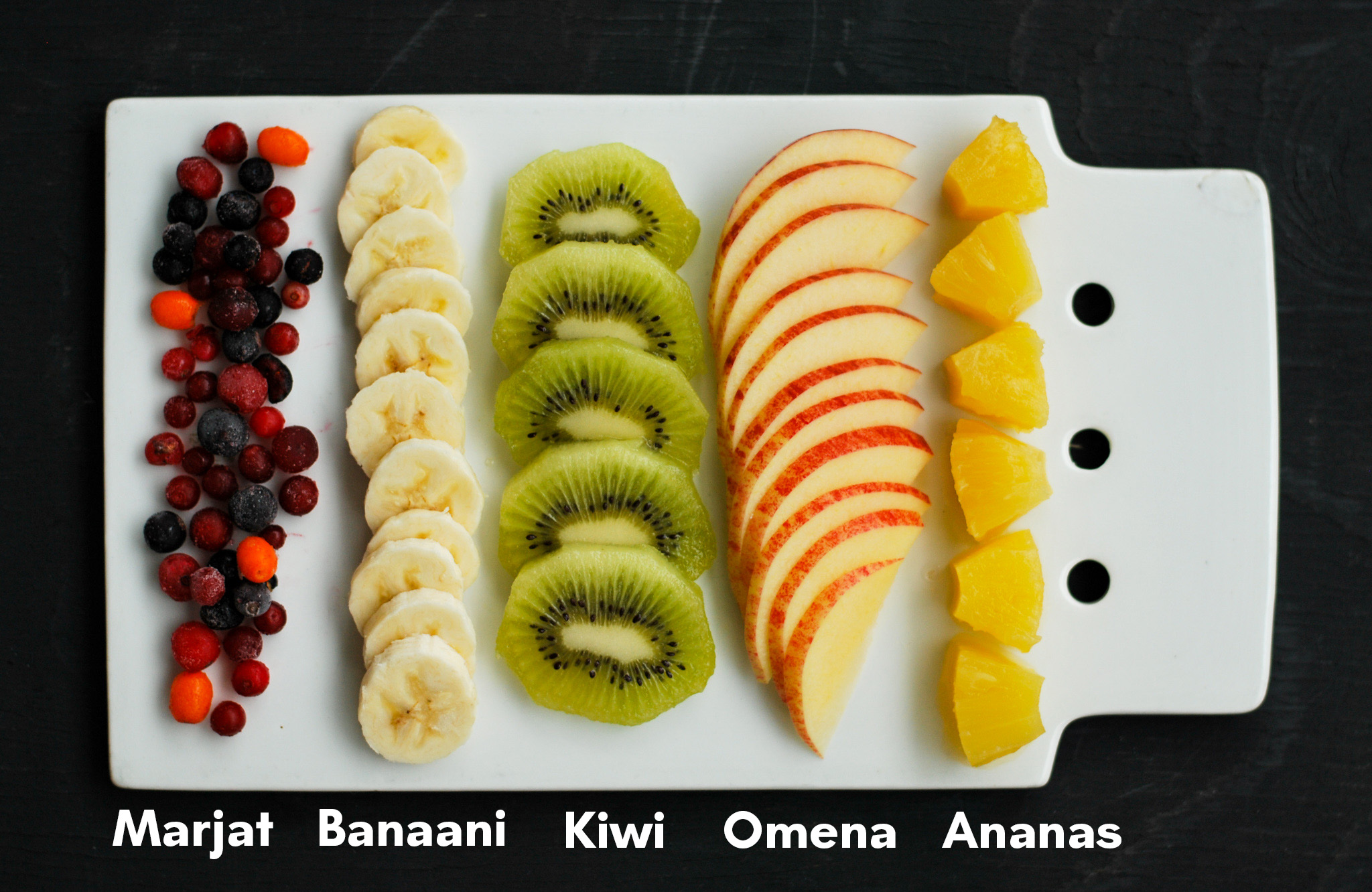 Kuvassa on valkoisen leikkuulaudan päällä viipaloituja hedelmiä kauniissa riveissä: marjoja, banaania, kiivejä, omenaa ja ananasta.