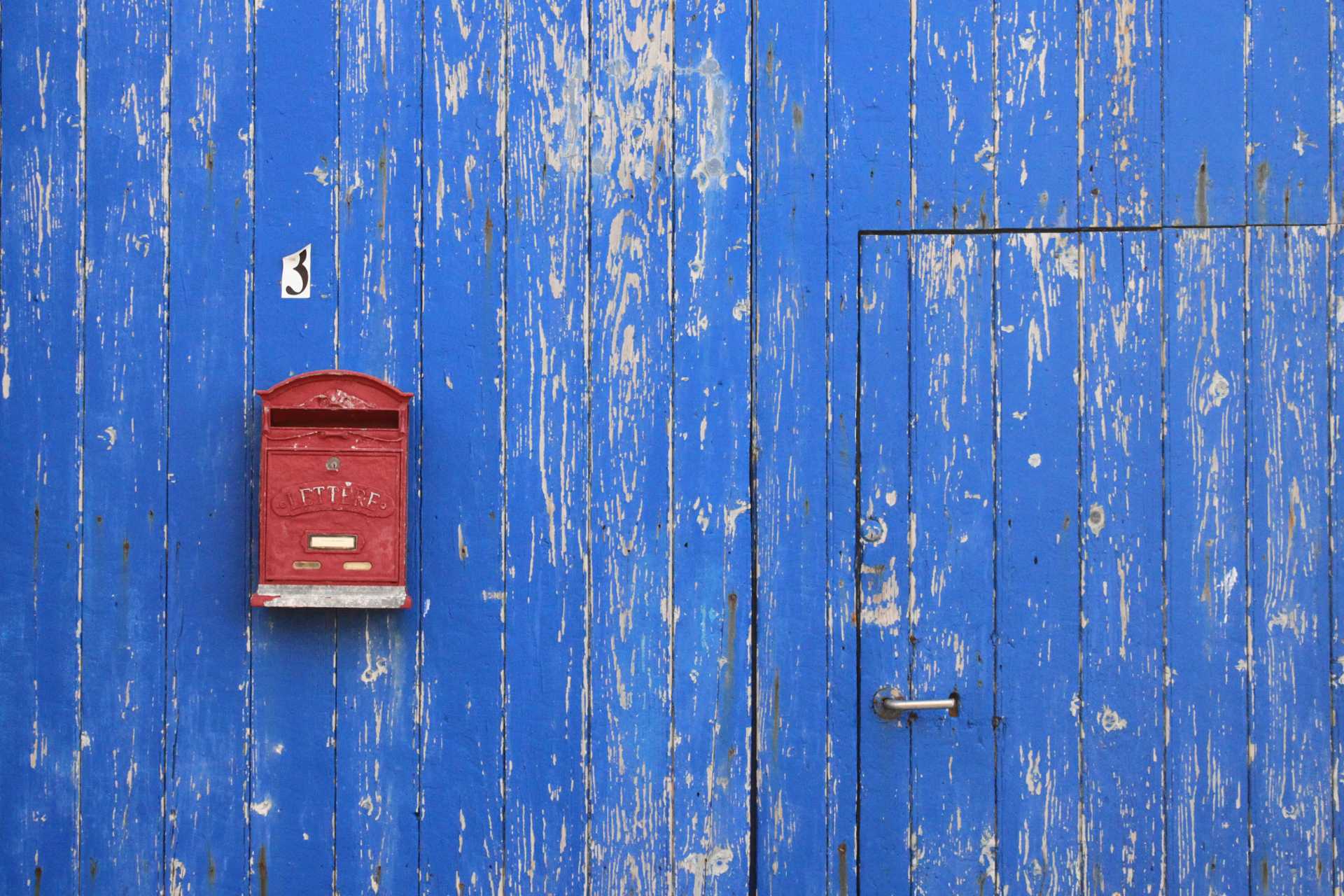 Epätasaisesti siniseksi maalatulla seinällä punainen postilaatikko
