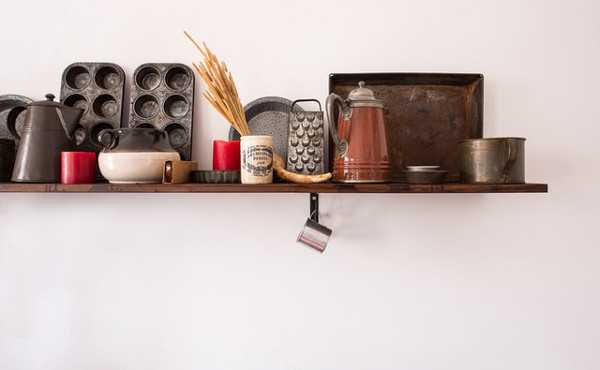 Kuvassa on vaalealla seinällä oleva hylly, jossa on muffinssipeltejä, kahvipannu, raastin, spagettia mukissa ja monenlaisia metallisia pieniä kippoja ja mitta-astioita.