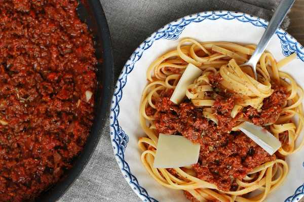 Kuvassa on lautasella spagettia ja soijarouhebolognesekastiketta. Lautasen vieressä on paistinpannulla lisää kastiketta.